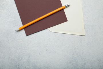 Empty brown square piece of paper, beige envelope and pencil on vintage white background. Empty space for text.