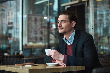 Portrait of pensive man tasting mug of delicious coffee while locating at table in confectionary shop. Rest concept