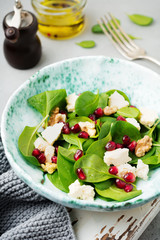 Fresh useful vegetarian wholesome spinach, pomegranate seeds, walnut, saffron, pepper and ricotta salad on  gray  background. Selective focus. Top view. Copy space for text.