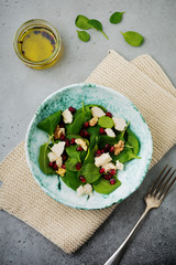 Fresh useful vegetarian wholesome spinach, pomegranate seeds, walnut, saffron, pepper and ricotta salad on  gray  background. Selective focus. Top view. Copy space for text.