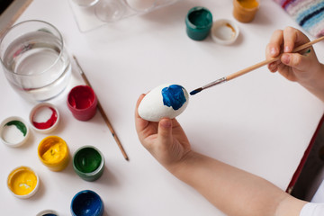 Children's hands paint Easter eggs. The child is drawing, step by step
