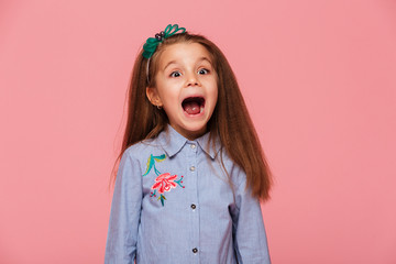 Joyous female kid in trendy shirt having fun shouting being excited and emotional over pink background