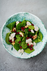 Fresh useful vegetarian wholesome spinach, pomegranate seeds, walnut, saffron, pepper and ricotta salad on  gray  background. Selective focus. Top view. Copy space for text.