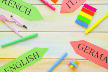 Learning Foreign Languages concept: paper arrows and bright school supplies on a light colored wooden background, close up, top view