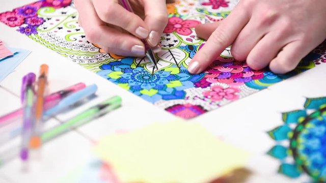 Color video of a young unrecognisable woman colouring in an adult colouring book. New art therapy and stress management trend. Close up shot, hand detail.