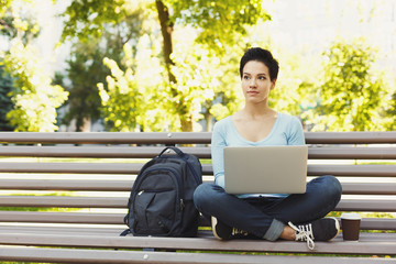 Young woman using laptop in park, copy space