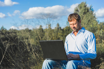 Man with pc  laptop sitting on grass in nature.