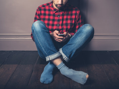 Young man with smart phone on wooden floor
