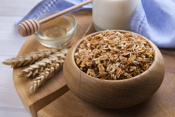 A wooden bowl of trail mix with almonds, raisins, seeds, cashew, hazelnut nuts, glass of milk and honey on white table. Vegetarian dietary sports nutrition. Close up, top view, copy space, background.