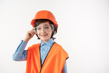 Portrait of smiling little boy trying himself as a construction manager. He is wearing safety glasses. Copy space in right side. Isolated on background