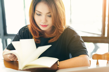 Asian stylish glasses woman designer wear black dress and red lips happiness reading a notebook in selective focus..