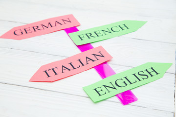 Learning Foreign Languages concept: German, English, Italian, French paper arrows on a light colored wooden background, close up, top view