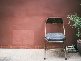 Fototapeta na wymiar Old cheap rusty chair with plant by grunge brown wall.