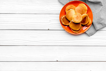 Homemade pancakes on orange plate. White wooden background top view copy space