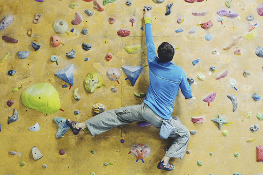 Young man practicing rock-climbing on a rock wall indoors.