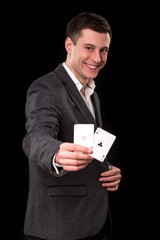 Young caucasian man wearing suit holding two aces in his hand on black background. Gambling concept. Casino