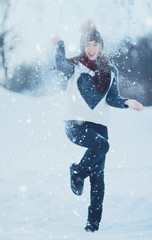 Cute young woman having fun in winter park on a bright day and playing with snow