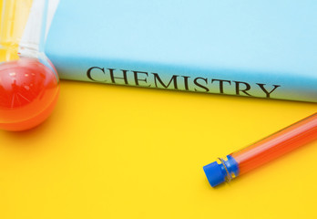 Education concept: Chemistry student's book and test tubes with red liquid on a bright yellow background with copy space