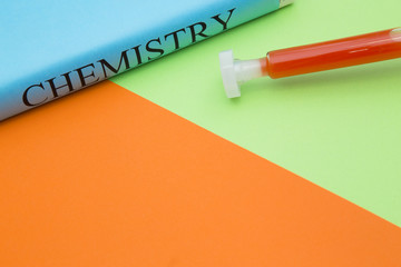Education concept: Chemistry student's book and test tube with red liquid on a bright orange and green background with copy space