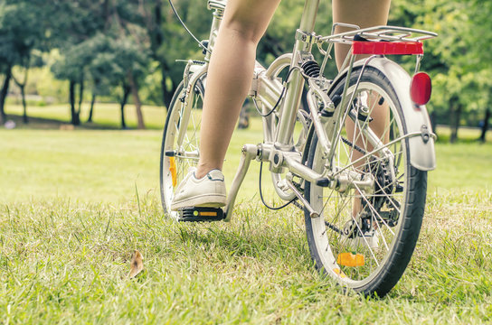 Detail of young woman's feet in sneakers riding on bike in green field