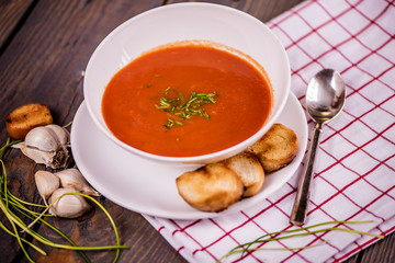 tomato soup  with pasta and chives and bread crouton in white plate on wood table 