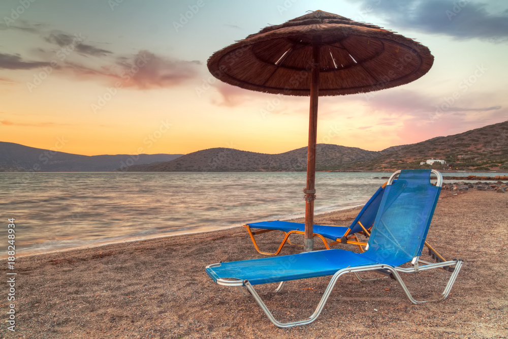 Poster Beach with parasol at Mirabello Bay at sunset, Greece