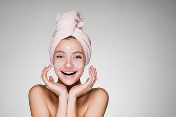 happy smiling girl with pink towel puts on face moisturizing white cream