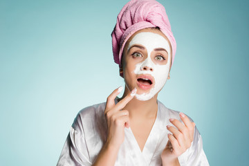 funny young girl with a pink towel on her head puts a white moisturizing mask on her face