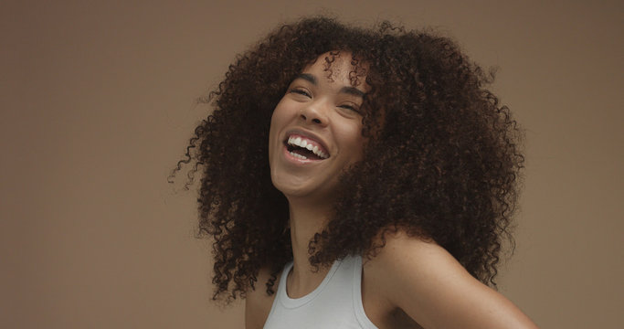 mixed race black woman portrait with big afro hair, curly hair in beige background. Natural laughing