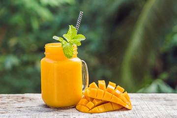 Mango smoothie in a glass Mason jar and mango on a green background. Mango shake. Tropical fruit concept