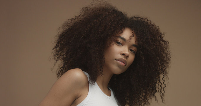 mixed race black woman portrait with big afro hair, curly hair in beige background