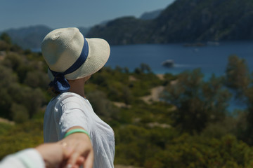 Obraz premium Young girl in hat holding an unknown man's hand and calling after him to enjoy the beautiful nature and the sea while on sunny summer day