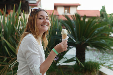 Fototapeta premium Portrait of beautiful positive young woman eating ice cream on background of palm trees.