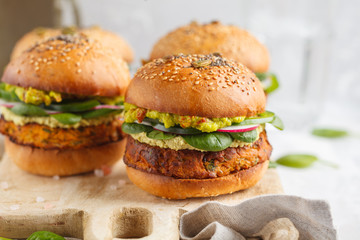 Healthy baked sweet potato burger with whole grain bun, guacamole, vegan mayonnaise and vegetables on a wooden board. Vegetarian food concept, light background.