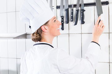 Female chef in uniform in industrial kitchen taking knife from wall bracket