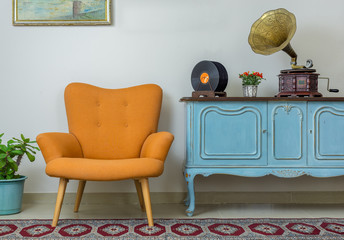 Vintage interior of retro orange armchair, vintage wooden light blue sideboard, old phonograph (gramophone), vinyl records on background of beige wall, tiled porcelain floor, and red carpet - obrazy, fototapety, plakaty