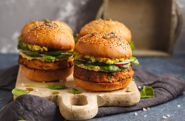 Healthy baked sweet potato burger with whole grain bun, guacamole, vegan mayonnaise and vegetables on a black slate board. Vegetarian food concept, dark background.