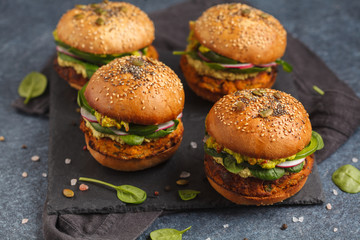 Healthy baked sweet potato burger with whole grain bun, guacamole, vegan mayonnaise and vegetables on a black slate board. Vegetarian food concept, dark background.