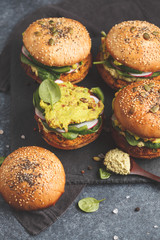 Healthy baked sweet potato burger with whole grain bun, guacamole, vegan mayonnaise and vegetables on a black slate board. Vegetarian food concept, dark background.