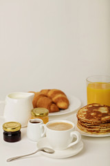 Breakfast - coffee with croissants, juice with pancakes on a white background.