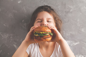 The little girl is eating a healthy baked sweet potato burger with a whole grains bun, guacamole,...