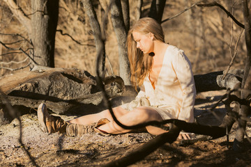Close up of young mixed race woman in white dress playing with hair near forest destroyed by wildfire while covered in ashes