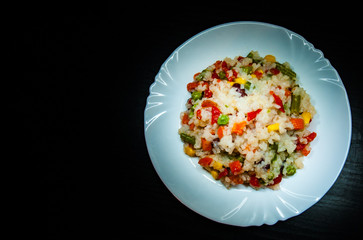 Rice with mixed vegetables on white plate  
 on dark wooden background with copy space.
