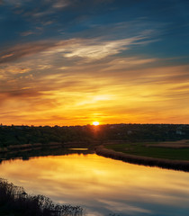 Fototapeta premium orange sunset in dramatic clouds over river
