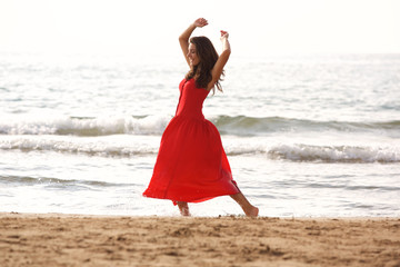 Fototapeta na wymiar Full length beautiful woman in red dress dancing alone on beach