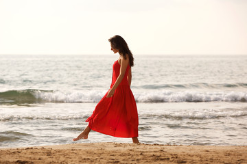 Fototapeta na wymiar Full length beautiful woman in red dress walking alone on beach