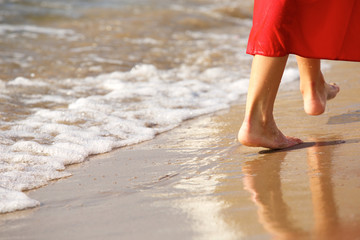 Close up woman in red walking barefoot on beach by waves