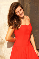 Fototapeta premium Beautiful woman in red dress leaning on wall smiling