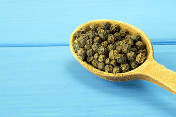 Black pepper in a wooden spoon on a blue background