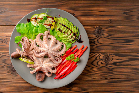 Top Down Of Octopus Served With Sliced Avocado, Lettuce, Red Pepper, Lime, Cucumber And Sprig Of Pea Leaves On Plate, Natural Seafood, Copy Space